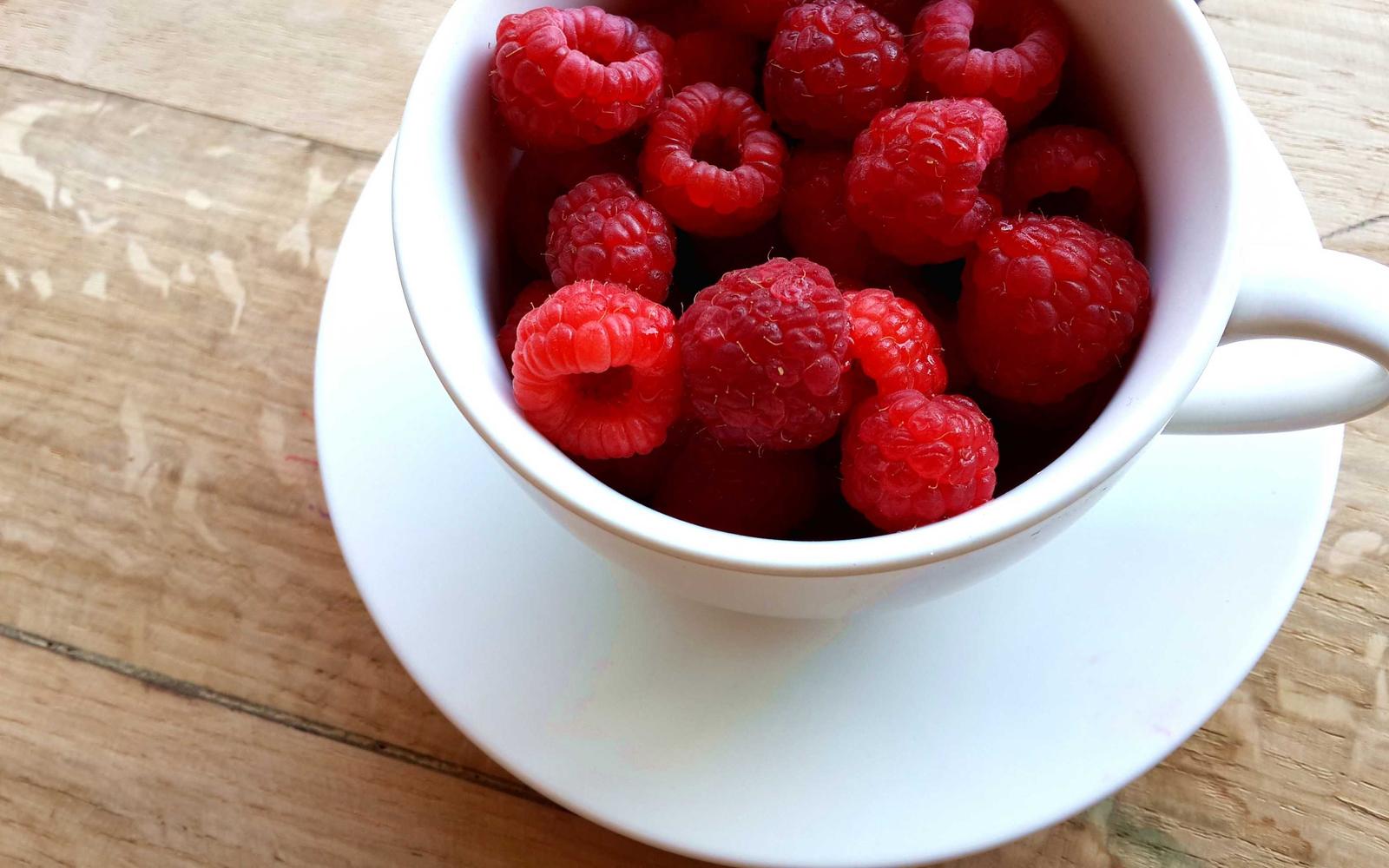 Raspberries piled in a white teacup