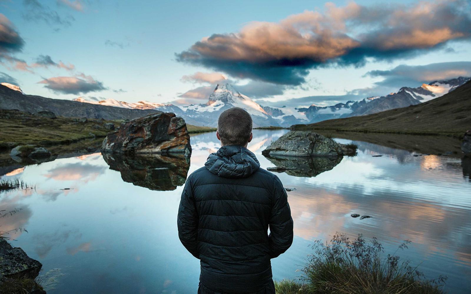 Hiker at a mirror-still alpine lake below the Matterhorn
